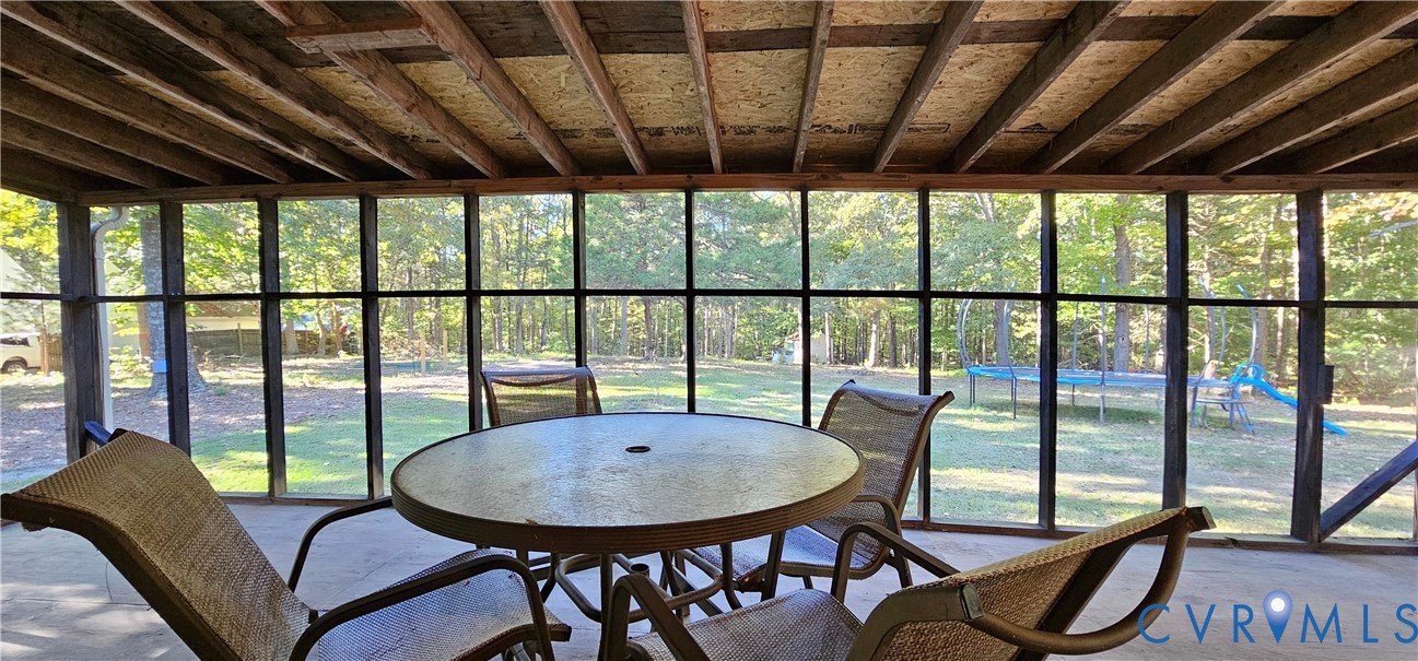 Screened porch featuring an exposed wood-beam ceiling, concrete flooring, and metal-frame screen panels