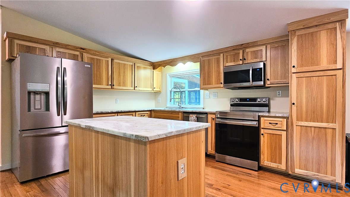 Kitchen featuring natural wood cabinetry, stone-finish countertops, stainless steel appliances, a center island, and wood-finish flooring