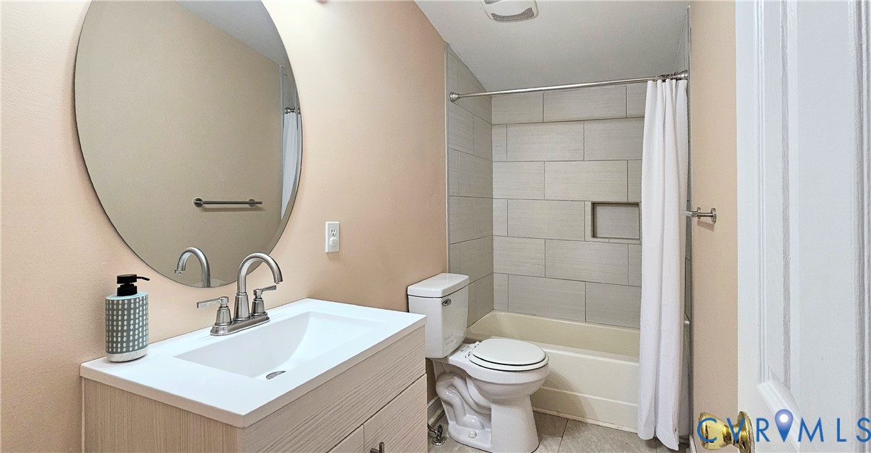 Vanity with a solid surface countertop, integrated sink, and metallic faucet, complemented by an oval wall-mounted mirror, ceramic tile shower surround with a built-in recessed niche, and tile flooring