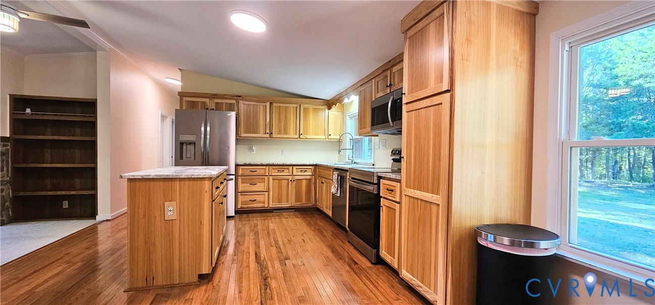 Kitchen featuring wood-finish cabinetry, a central island with a stone-surface countertop, stainless steel appliances, wood-finish flooring, and built-in shelving