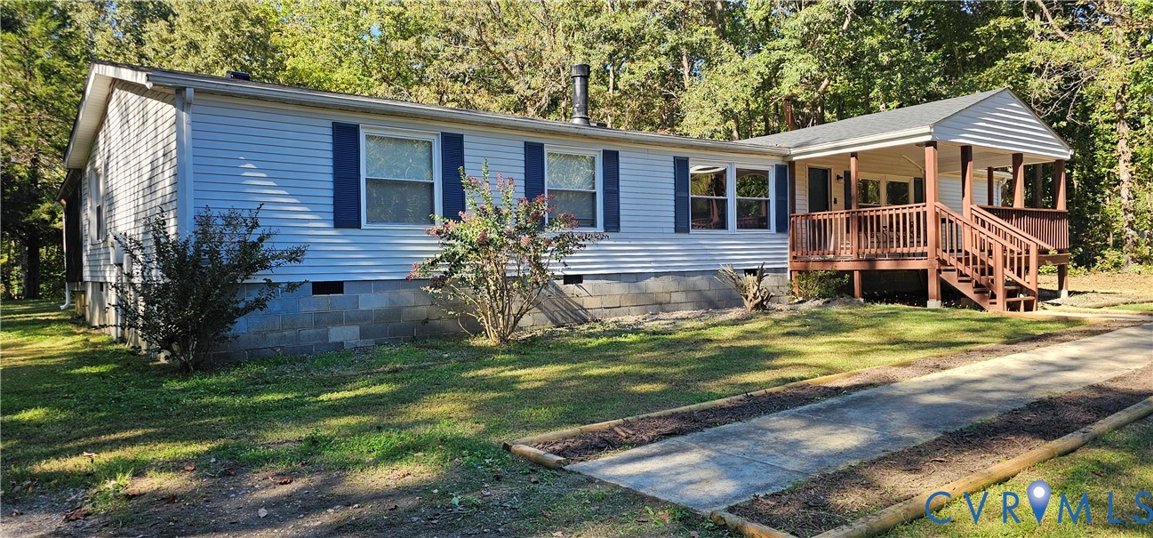 Light-colored horizontal siding exterior featuring dark blue window shutters, a concrete masonry unit foundation, and a raised wooden front deck with railings Light-colored horizontal siding exterior featuring dark blue window shutters, a concrete masonry unit foundation, and a raised wooden front deck with railings