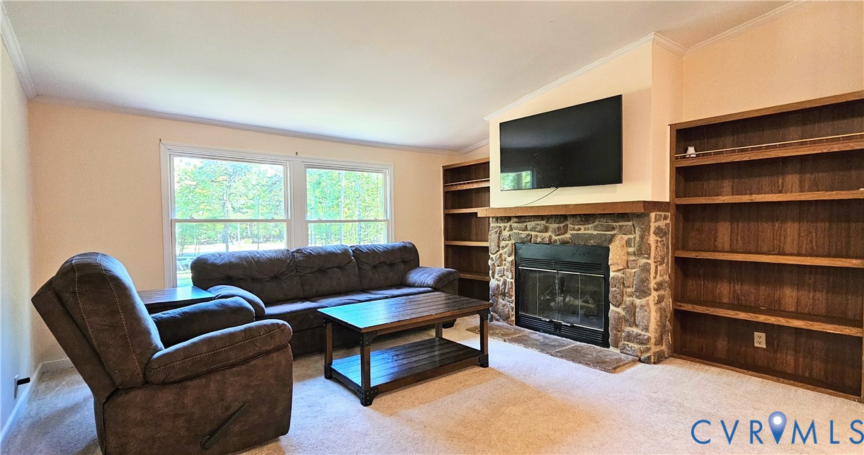 Living area featuring a floor-to-ceiling stone fireplace, wood-finish built-in shelving, and large double-pane windows