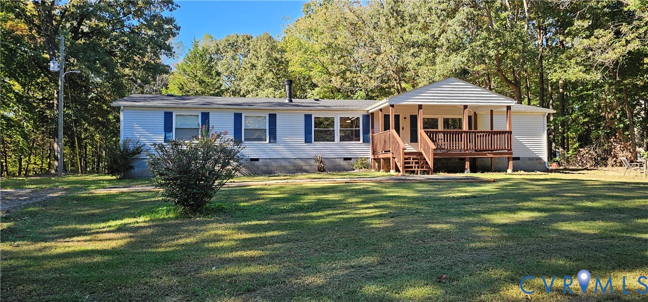 Single-story residence featuring light-colored siding, blue window shutters, a covered front porch with wooden railings, and a large yard surrounded by mature trees