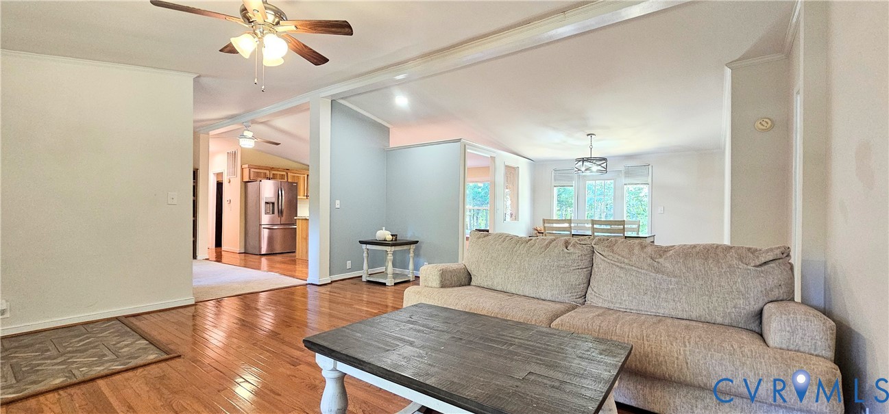 Open-concept interior featuring wood-finish flooring, vaulted ceilings, a ceiling fan with integrated lighting, and a multi-light drum chandelier