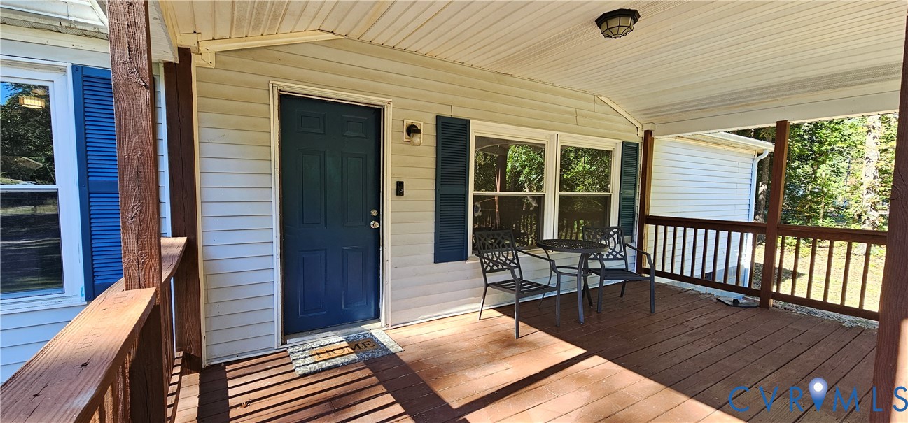 Covered porch featuring wood-plank decking, a solid-panel entry door, vinyl siding, and wooden railings