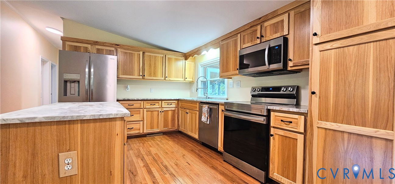 Kitchen featuring wood cabinetry, stainless steel appliances, an island with stone-finish countertops, and wood-finish flooring
