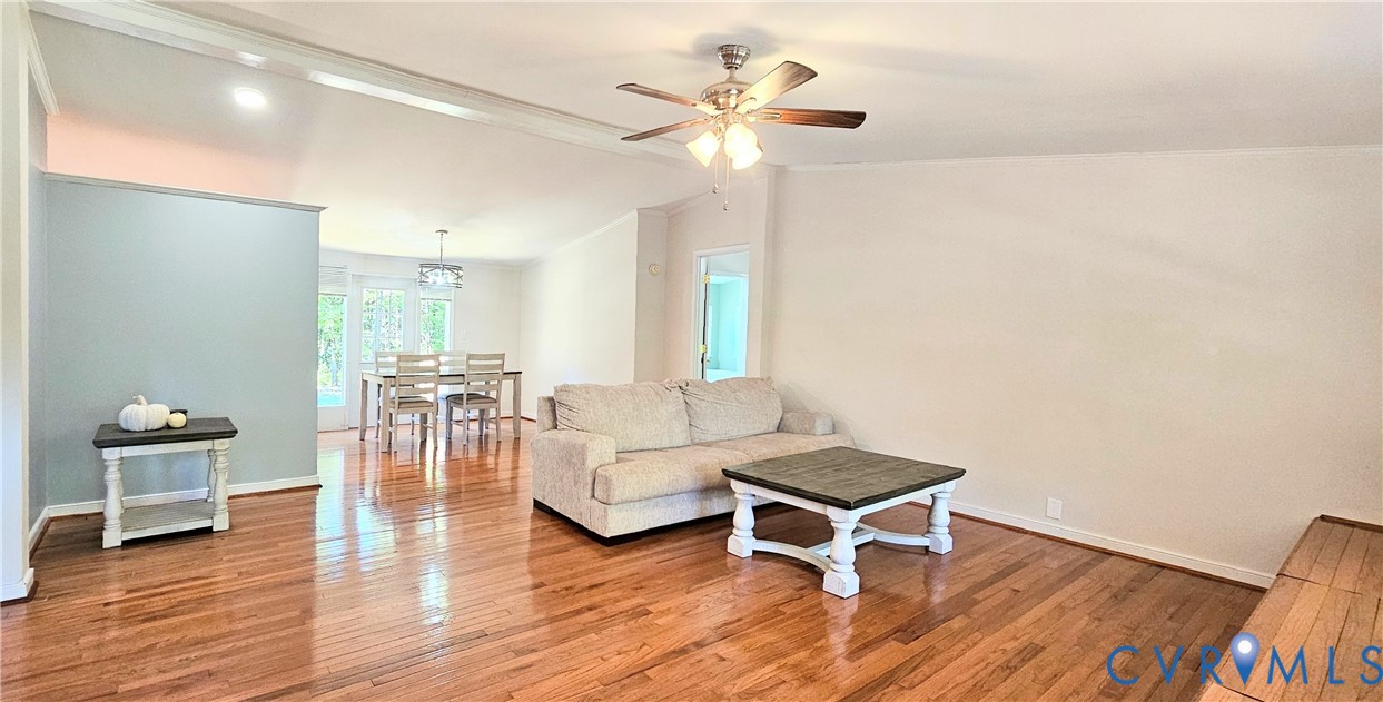 Open-concept interior featuring wood-finish flooring, a ceiling fan with integrated lighting, an accent wall, and a multi-light chandelier