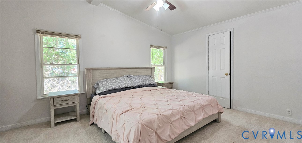 Vaulted ceiling featuring a central lighted ceiling fan, neutral wall-to-wall carpeting, two multi-pane windows, and a six-panel interior door