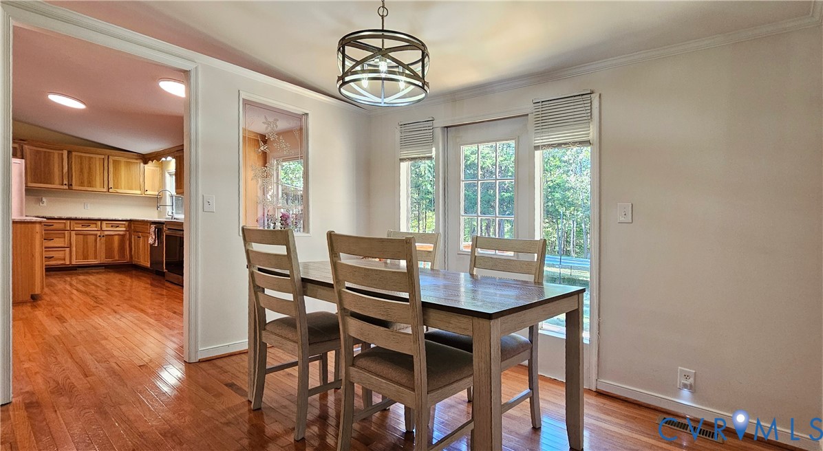 Dining area featuring wood-finish flooring, a drum-style chandelier, a pass-through wall window, and a glass-paned door providing outdoor visibility