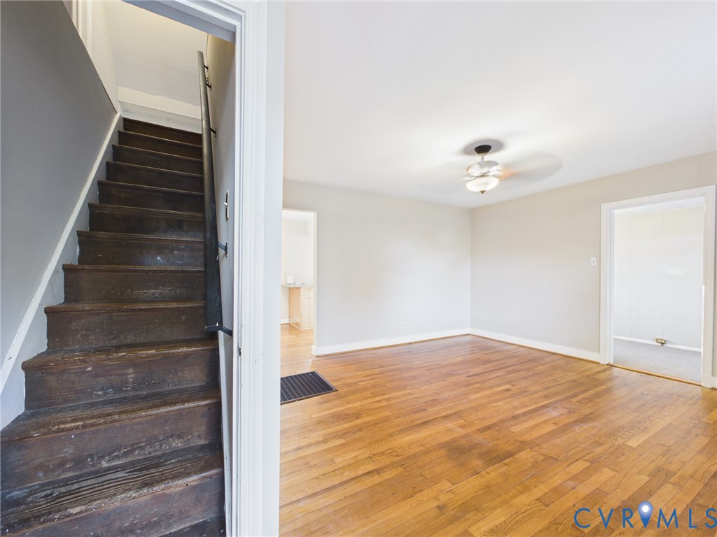 Wood-finish flooring, staircase with a metal handrail, ceiling-mounted light fixture with fan, and neutral wall tones