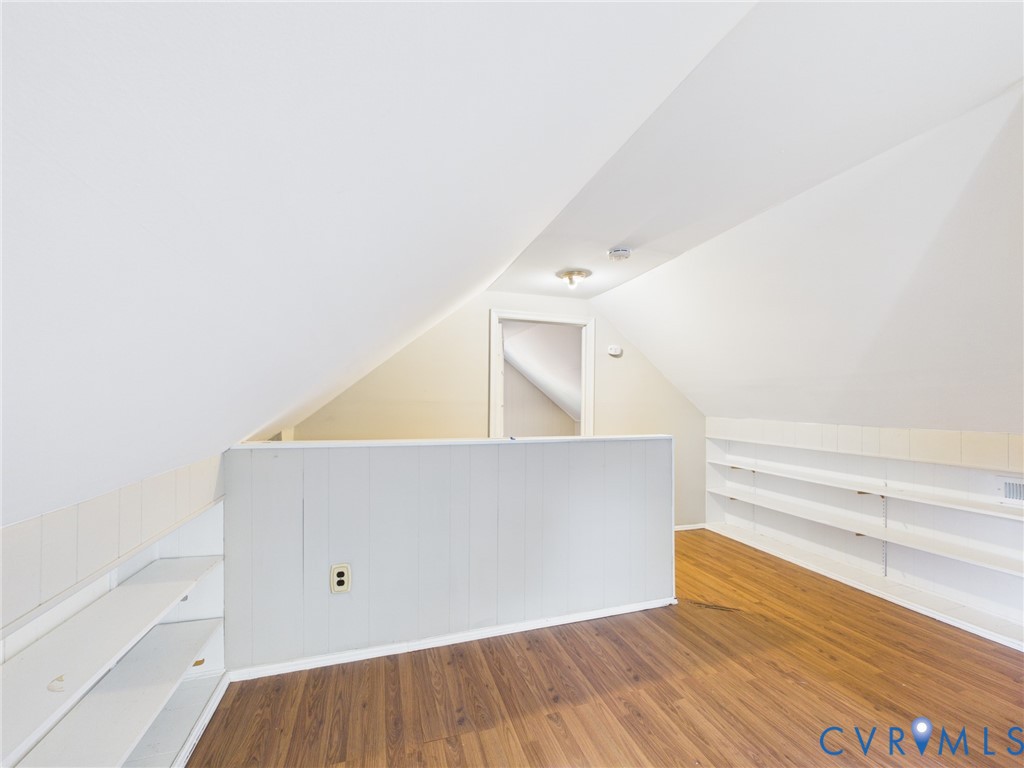 Finished attic space featuring vaulted ceilings, wood-finish flooring, and extensive built-in shelving