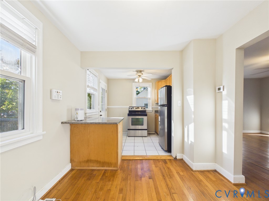 Kitchen area featuring wood cabinetry, stainless steel appliances, stone-surface breakfast bar, ceramic tile flooring, and wood-finish flooring
