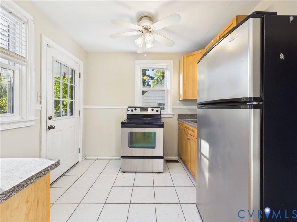 Kitchen featuring wood cabinetry, stainless steel appliances, white ceramic tile flooring, and a ceiling-mounted light fixture with integrated fan