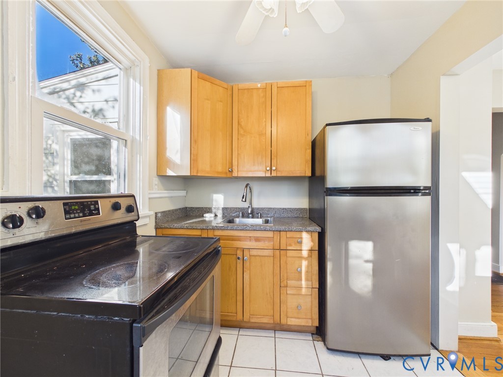 Kitchen featuring light wood cabinetry, stone-finish countertops, stainless steel refrigerator, black electric range, and tile flooring