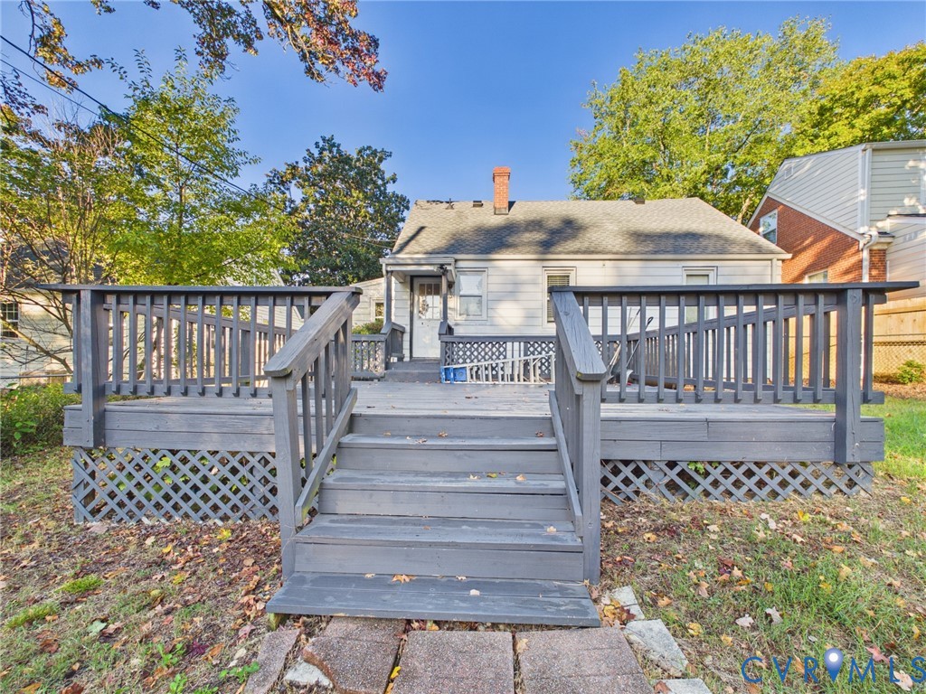 Elevated wooden deck featuring railing, lattice skirting, and central stairs leading to the rear exterior of the home