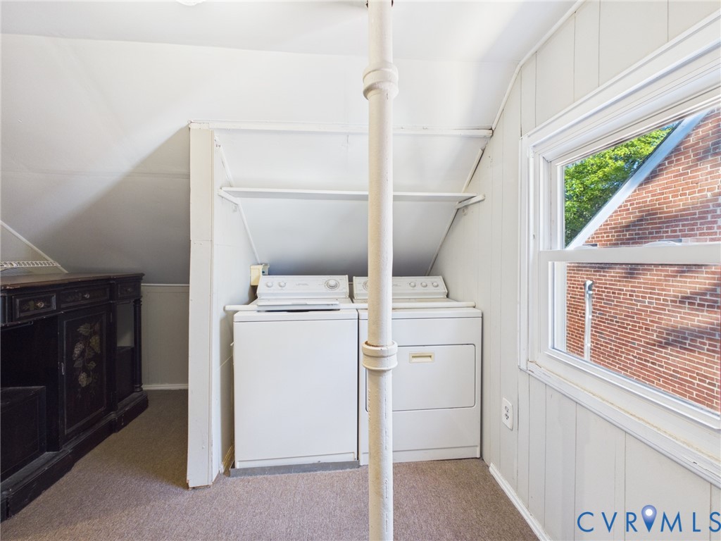 Laundry area featuring white washer and dryer units, built-in shelving, vertical wood-paneled walls, and a large window