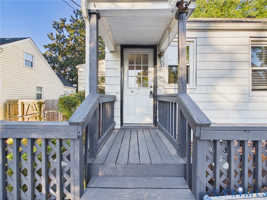 Exterior entry featuring horizontal lap siding, a covered porch, wood decking, and decorative lattice railing