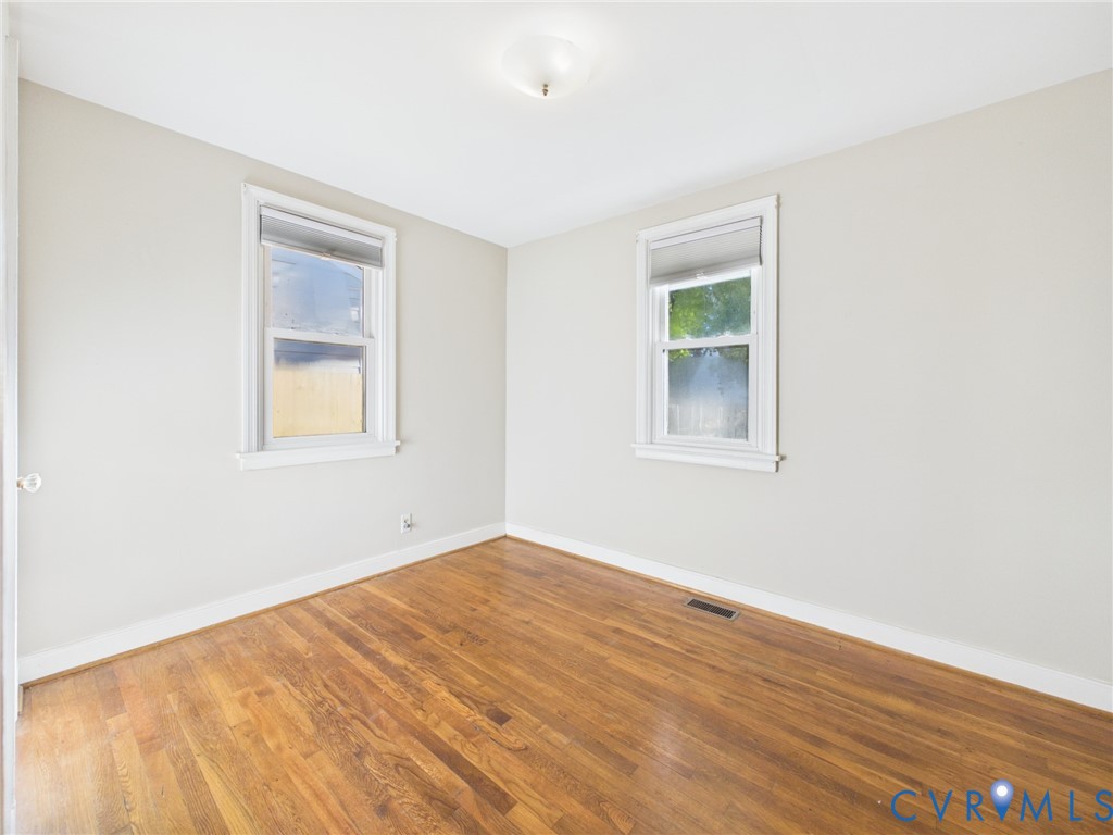 Room featuring wood-finish flooring, neutral-toned walls, and two double-hung windows with white trim
