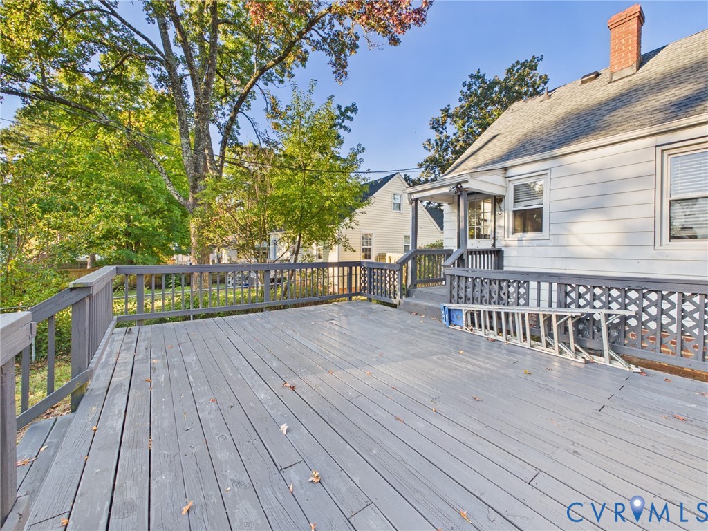 Expansive exterior wood deck featuring railing with lattice detailing, horizontal siding, and brick chimney
