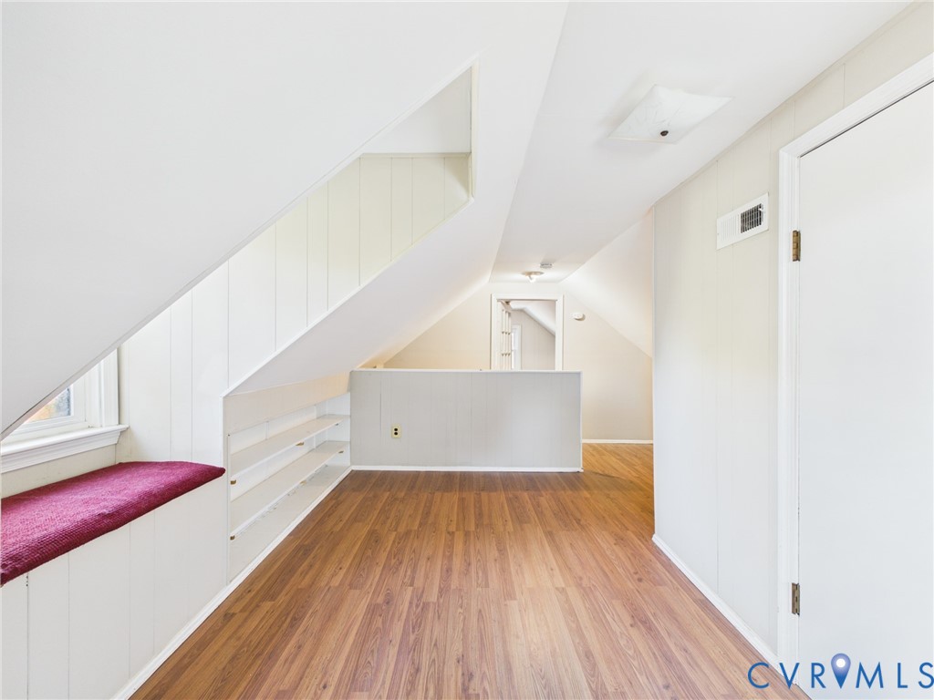 Sloped ceilings with wood-finish flooring, built-in shelving, and a window bench