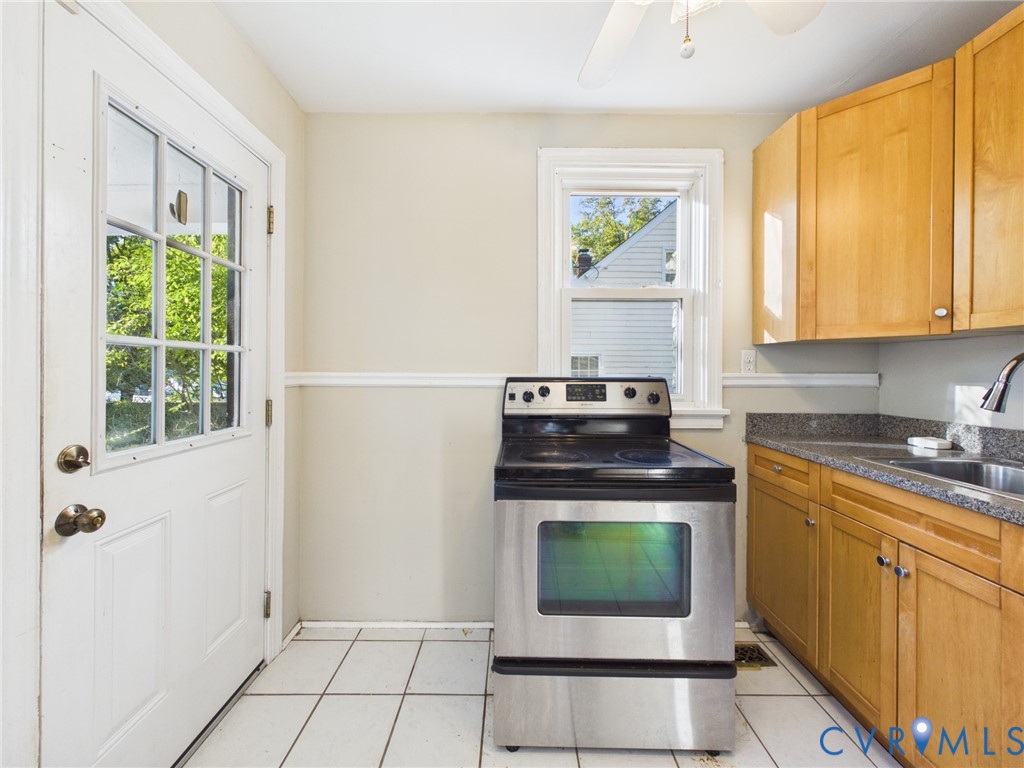Kitchen featuring light wood cabinetry, stone-finish countertops, a stainless steel range, ceramic tile flooring, and a glass-paneled exterior door