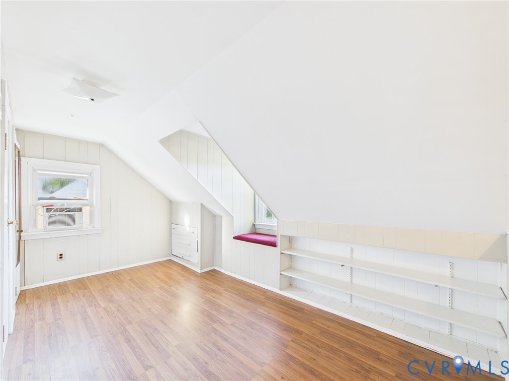 Room featuring wood-finish flooring, built-in shelving, vaulted ceilings, and a window seat