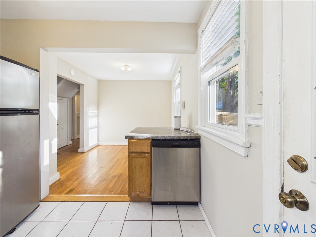 Kitchen featuring wood-finish flooring, white tiled flooring, stainless steel dishwasher, stainless steel refrigerator, and stone-surface countertop