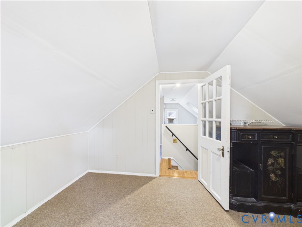 Attic space featuring vaulted ceilings, neutral carpeting, and a multi-pane glass door