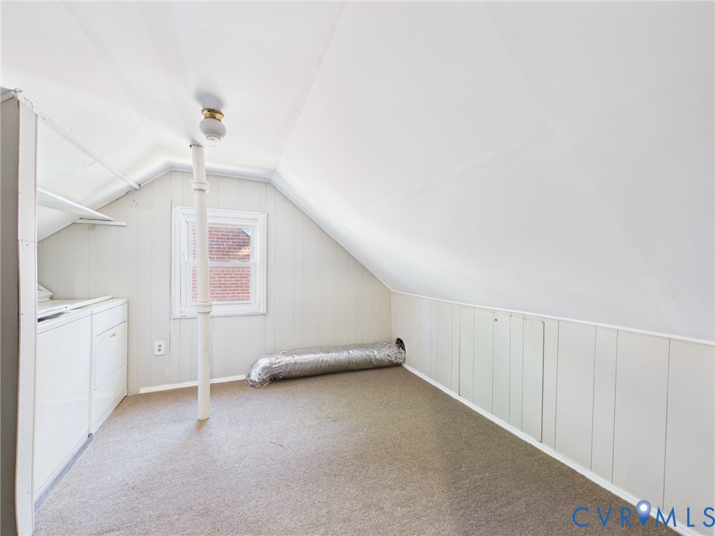 Attic space featuring vaulted ceilings, paneled walls, carpeting, a single-hung window, and a vertical support column
