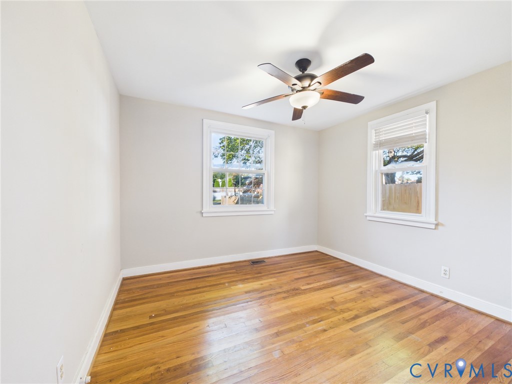 Room interior featuring wood-finish flooring, two windows with white trim, and a ceiling fan with integrated lighting