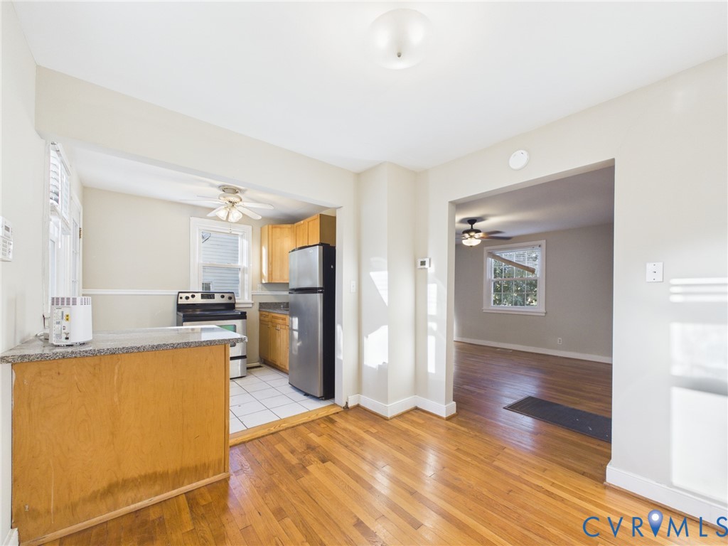 Kitchen featuring natural wood cabinetry, stone-finish countertops, stainless steel appliances, and white tile flooring, with wood-finish flooring extending into the additional living area