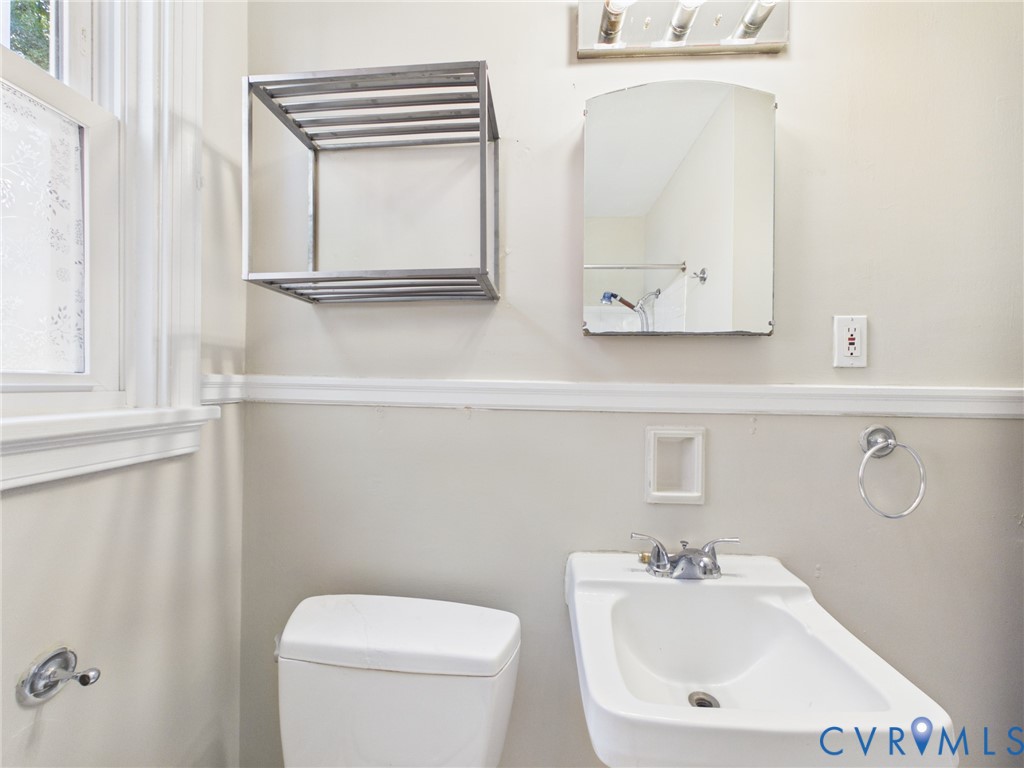Wall-mounted metal storage shelving, wall-mounted mirror, chrome-finished hardware, sink with dual-handle faucet, and chair-height toilet