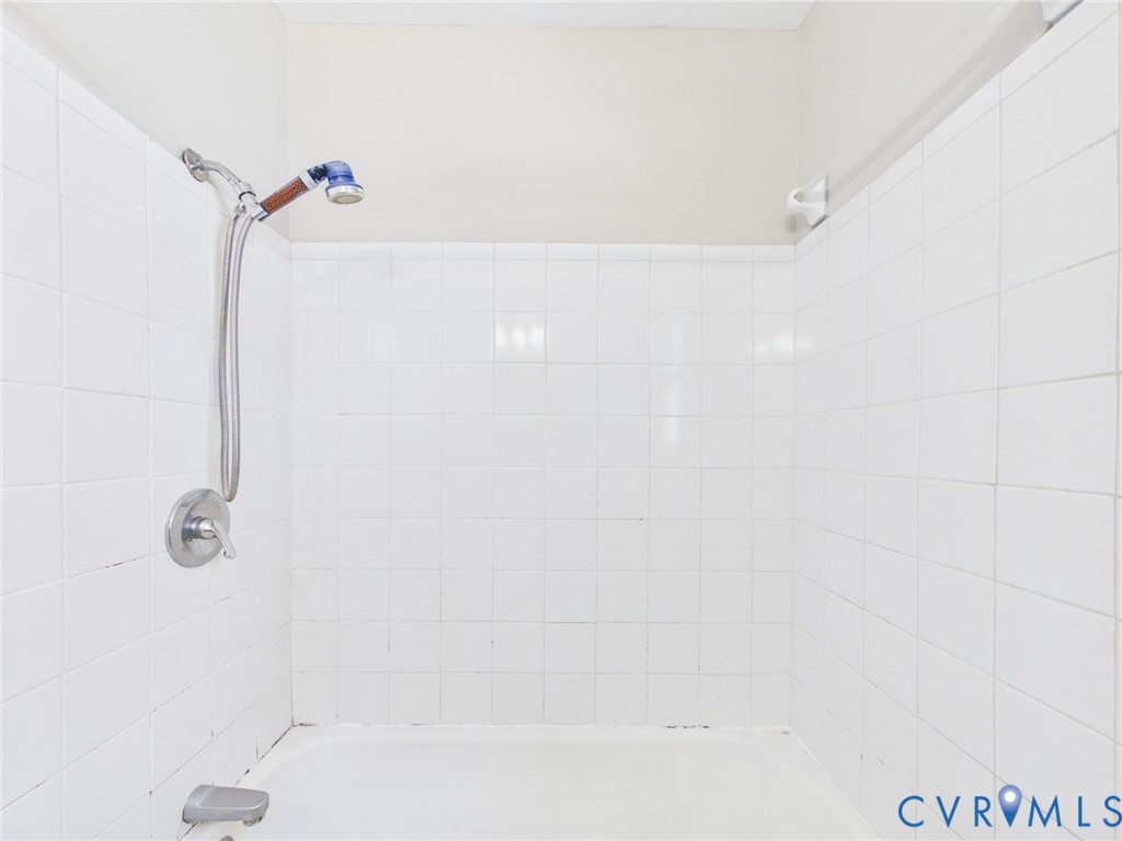 Full-height white square-tiled tub surround featuring a chrome-finish single-handle mixing valve, matching tub spout, and adjustable handheld shower head on a slide bar