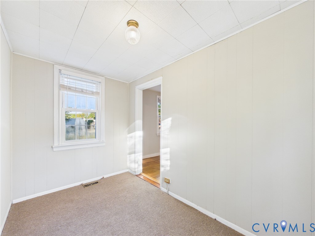 Interior room featuring wall paneling, a single-hung window with mini blinds, carpeted flooring, and a flush-mount ceiling light fixture