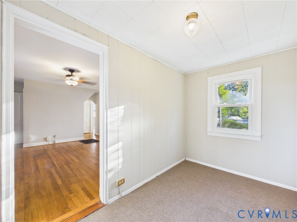 Interior room featuring paneling, carpeted flooring, a single-hung window with white casing, and a flush-mount ceiling light fixture