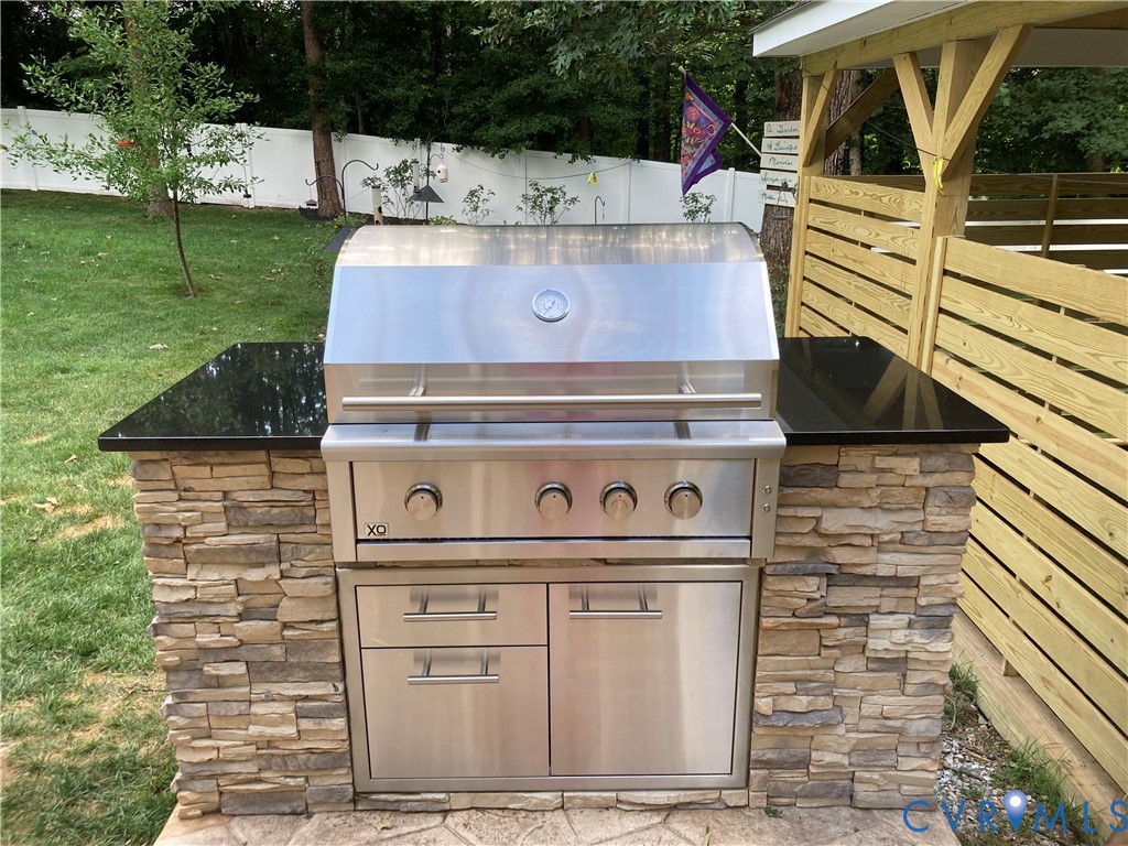 Outdoor kitchen island featuring an XO stainless steel gas grill, granite countertop, stacked stone base, and integrated stainless steel storage space. Outdoor kitchen island featuring an XO stainless steel gas grill, granite countertop, stacked stone base, and integrated stainless steel storage space.