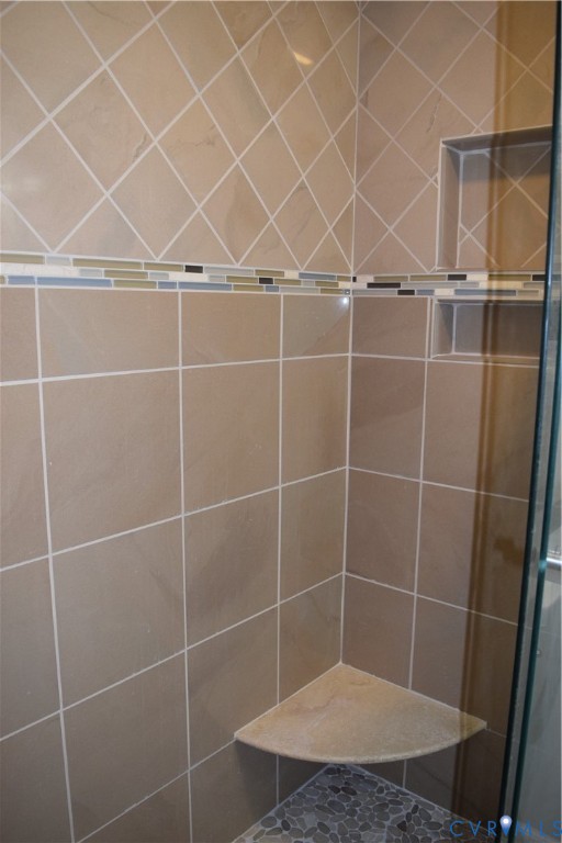 Shower enclosure featuring large-format wall tile, multi-colored glass tile inlay, a corner stone-finish bench, and recessed wall shelving.