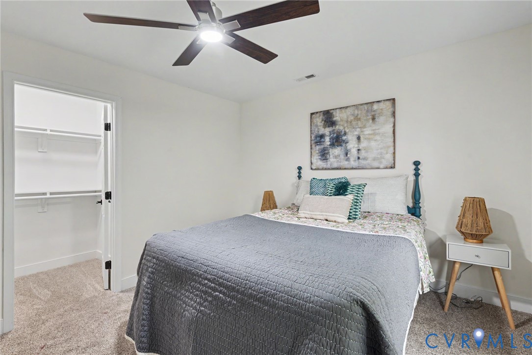 Neutral wall color, carpeted flooring, ceiling fan with integrated lighting, and a walk-in closet featuring wire shelving