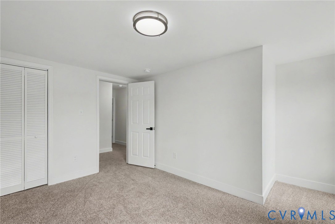Room featuring neutral carpeting, a semi-flush mount dome ceiling light, a bi-fold closet door, and a six-panel door with matte black hardware