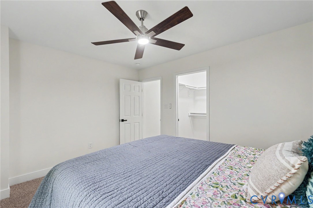 Ceiling fan with integrated lighting, neutral wall paint, carpeted flooring, and walk-in closet featuring built-in shelving