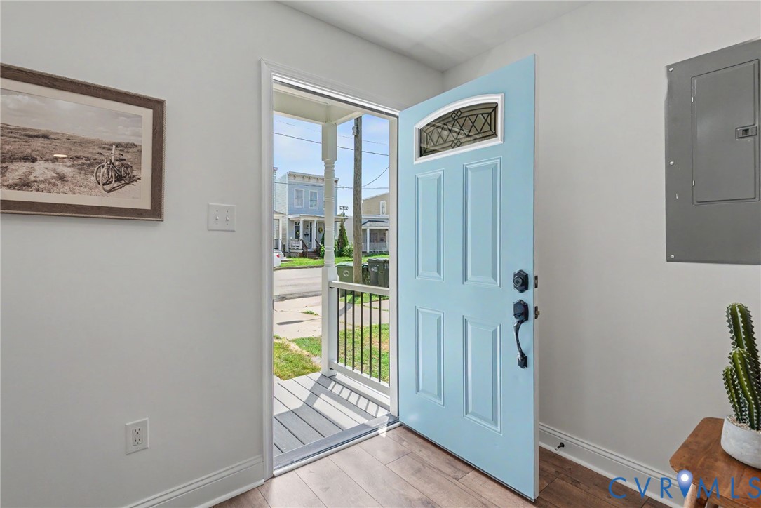Entryway featuring a light blue front door with a decorative arched transom window, wood-finish flooring, and a covered porch with a metal railing