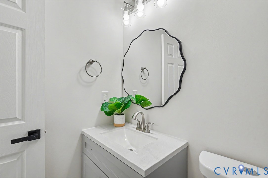 Vanity featuring a light-toned countertop, integrated basin, and brushed-nickel dual-handle faucet, accented by a scalloped-edge wall mirror and overhead multi-bulb vanity light
