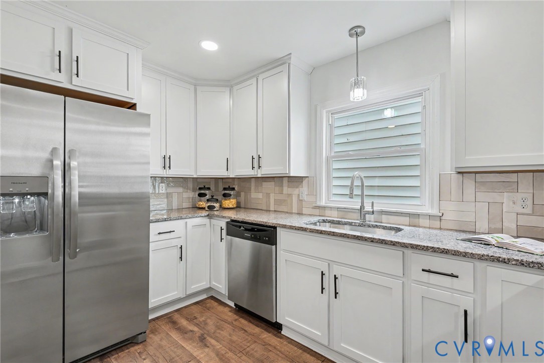 Kitchen featuring white shaker-style cabinetry, stainless steel appliances, stone-look countertops, herringbone-patterned tile backsplash, and wood-finish flooring