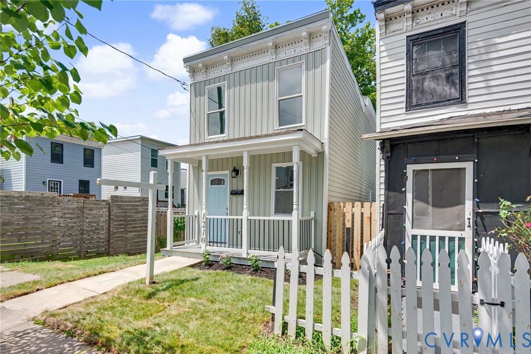 Two-story residence featuring vertical siding, decorative roofline corbels, an integrated front porch with turned columns, and a picket-style perimeter fence