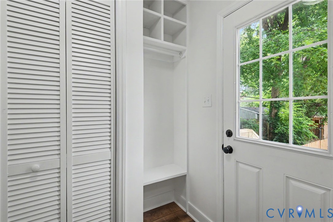 Built-in shelving unit with integrated bench seating, white louvered closet doors, wood-finish flooring, and a multi-pane glass door