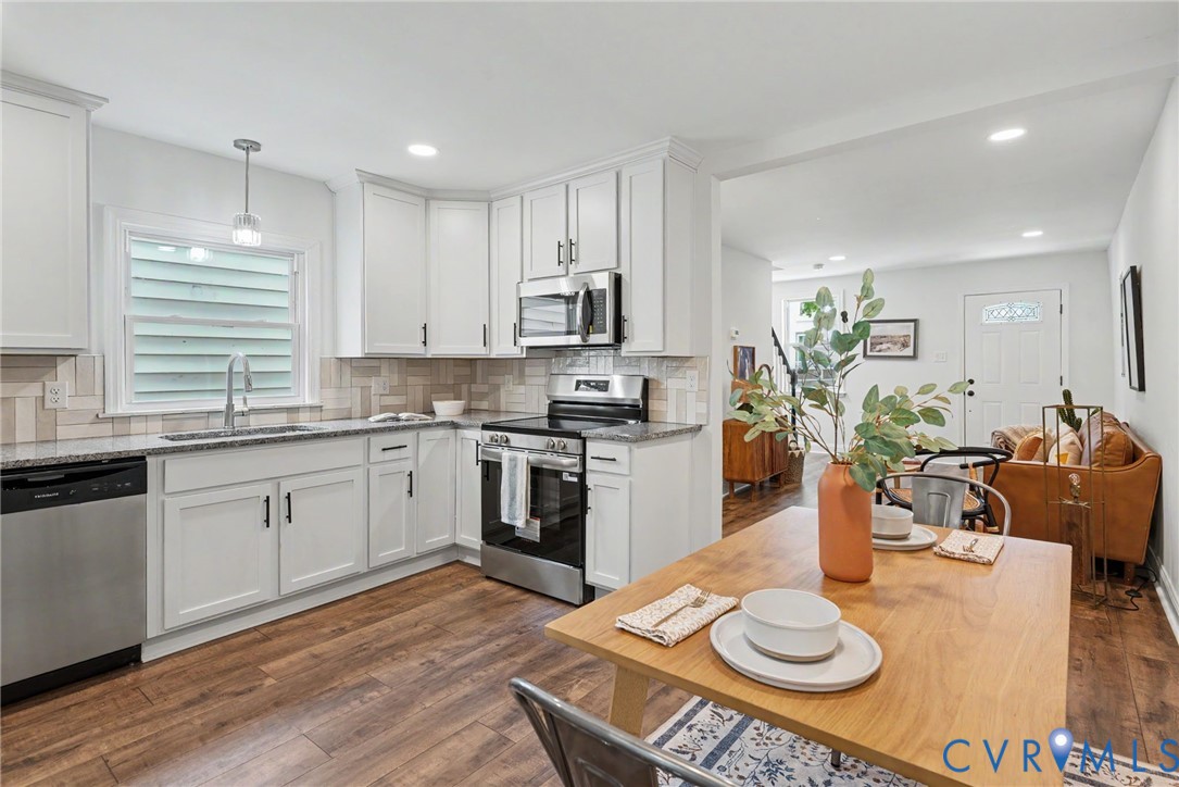Kitchen featuring white shaker-style cabinetry, stainless steel appliances, speckled stone-finish countertops, and a neutral tile backsplash, with wood-finish flooring extending throughout