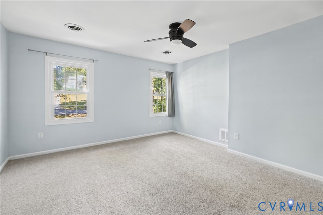 Neutral-toned interior featuring wall-to-wall carpeting, dual-pane windows with trim, and a ceiling fan