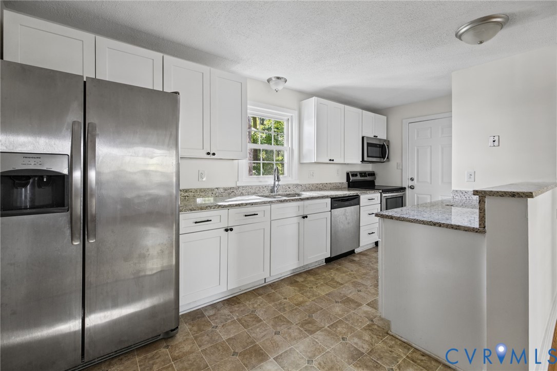 Kitchen featuring white cabinetry, stone-finish countertops, stainless steel appliances, and a pass-through breakfast bar Kitchen featuring white cabinetry, stone-finish countertops, stainless steel appliances, and a pass-through breakfast bar