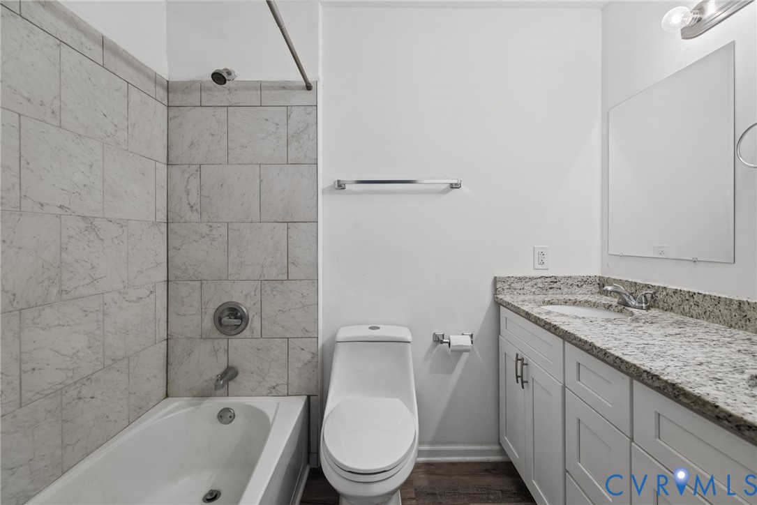 Bathroom featuring white cabinetry, stone-finish vanity countertop, under-mount sink, chrome fixtures, and a tub-shower combination with floor-to-ceiling tile surround