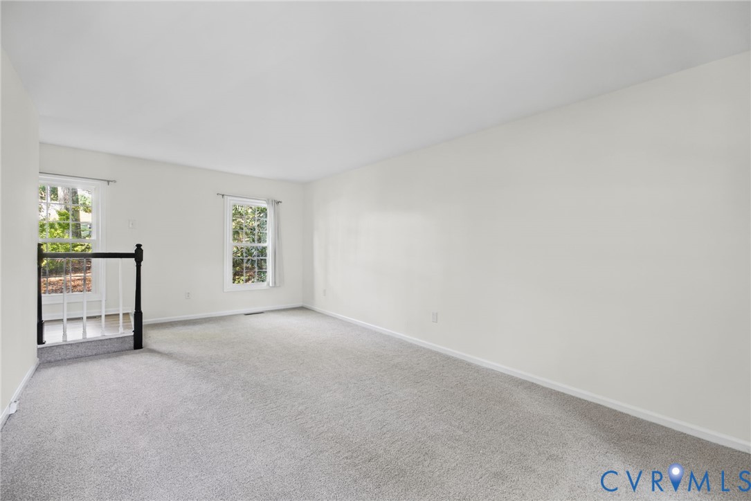 Neutral-toned wall paint, plush carpeting, multi-pane windows, and a staircase featuring a dark-finish wooden handrail with white balusters Neutral-toned wall paint, plush carpeting, multi-pane windows, and a staircase featuring a dark-finish wooden handrail with white balusters